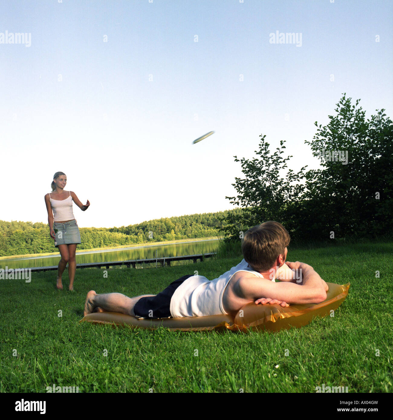young woman is playing frisbee and getting watched by a young man on a luma at a lake Stock Photo