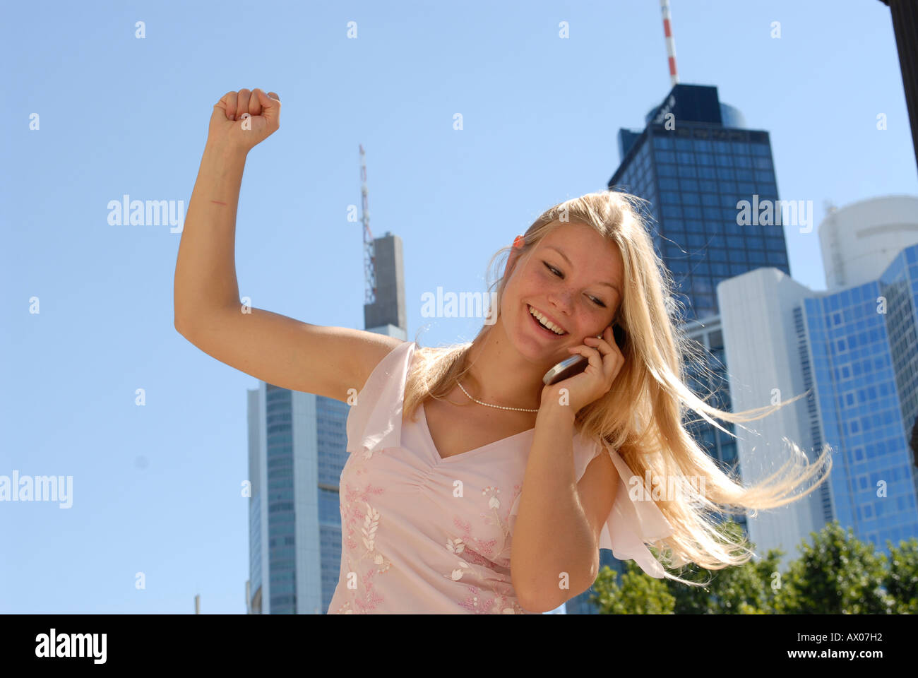 junge Frau blond lange Haare Stadt City Hochhaus Glasfassaden Teenager Handy mobile cellphone Telefon telefonieren Erfolg Emotio Stock Photo