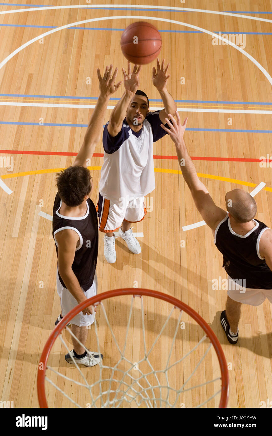 One basketball player shoots the basketball while two more players try to block his shot Stock Photo