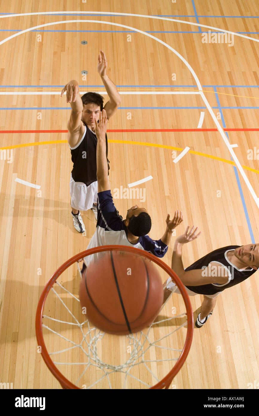 A basketball player shooting a basket and two more players playing defense Stock Photo