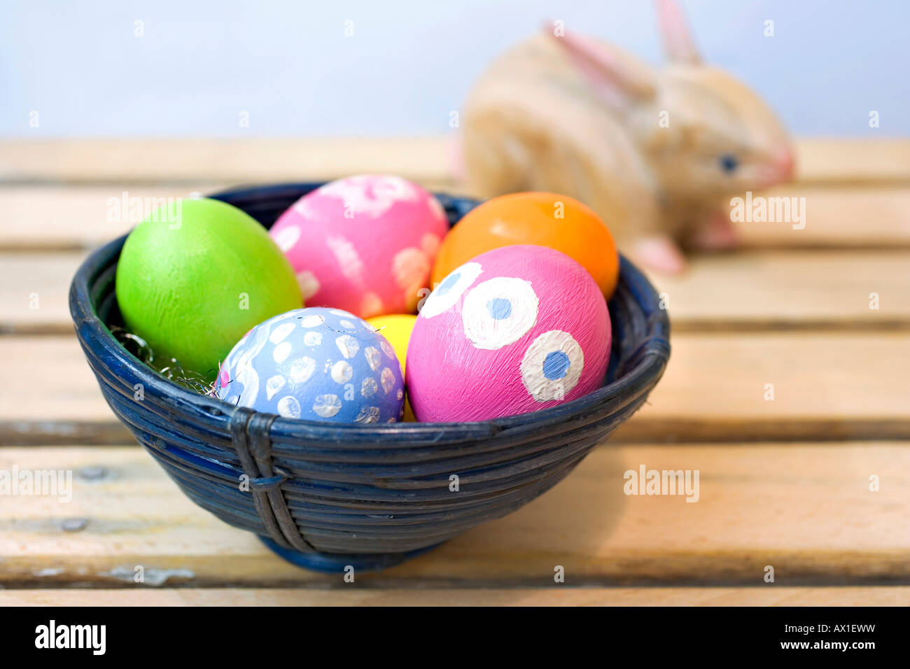 Hand-painted Easter eggs in a blue bamboo bowl beside wooden Easter bunny Stock Photo