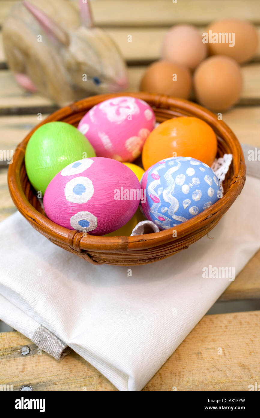 Hand-painted Easter eggs in a brown bamboo bowl beside a wooden Easter bunny Stock Photo