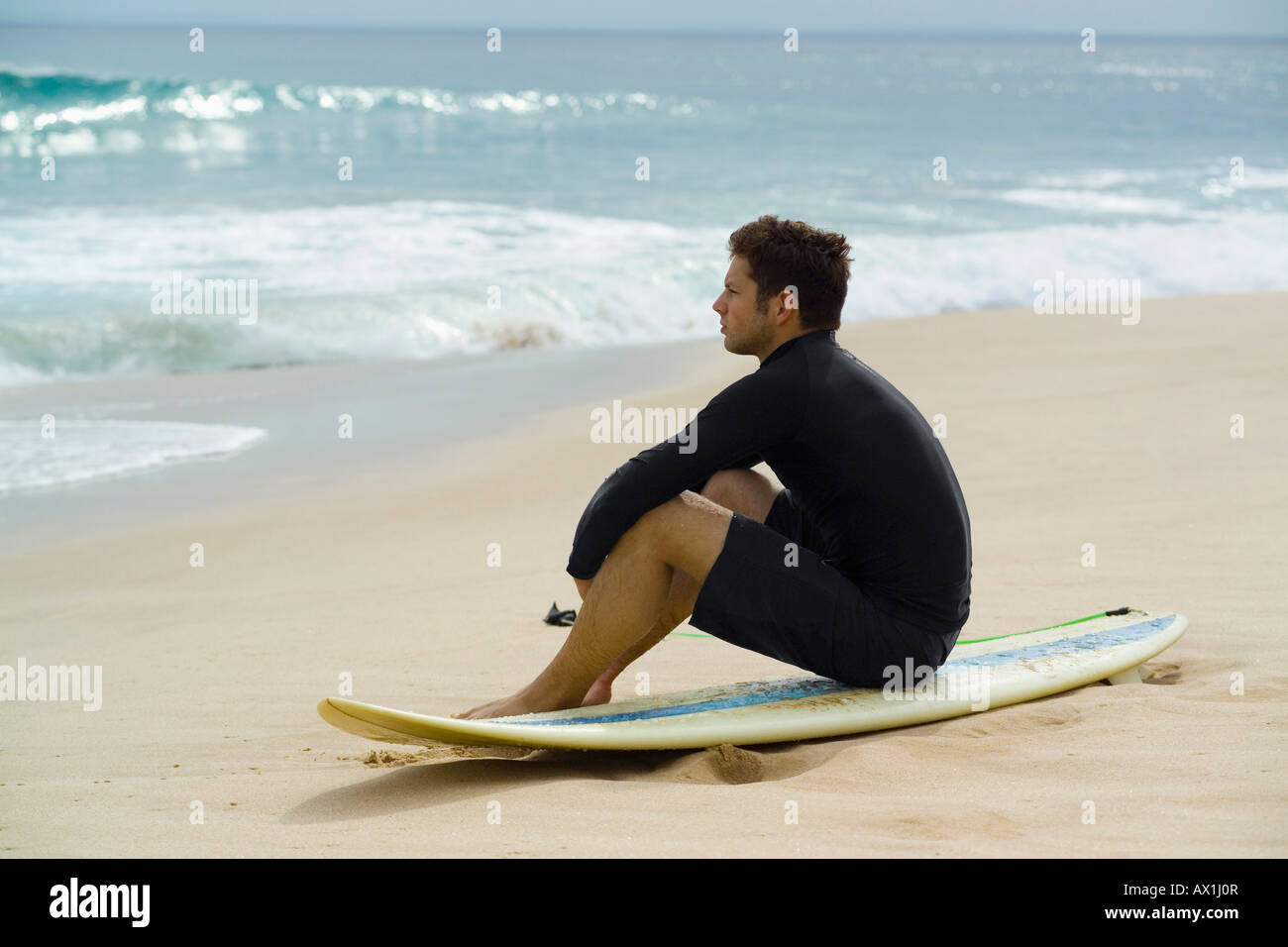 A surfer sitting on the beach Stock Photo
