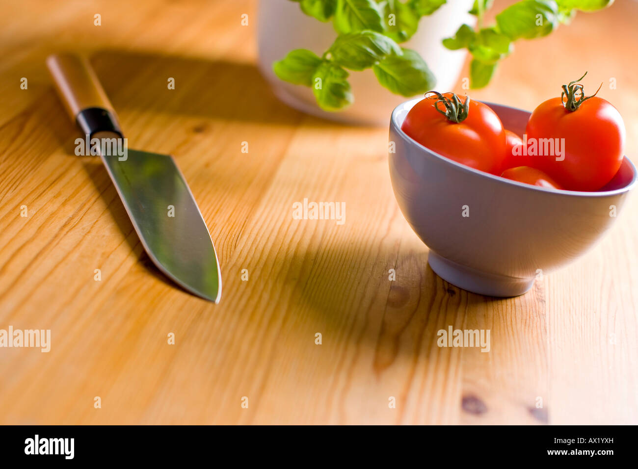 Kitchen knife laying beside tomatoes in a bowl with basil Stock Photo