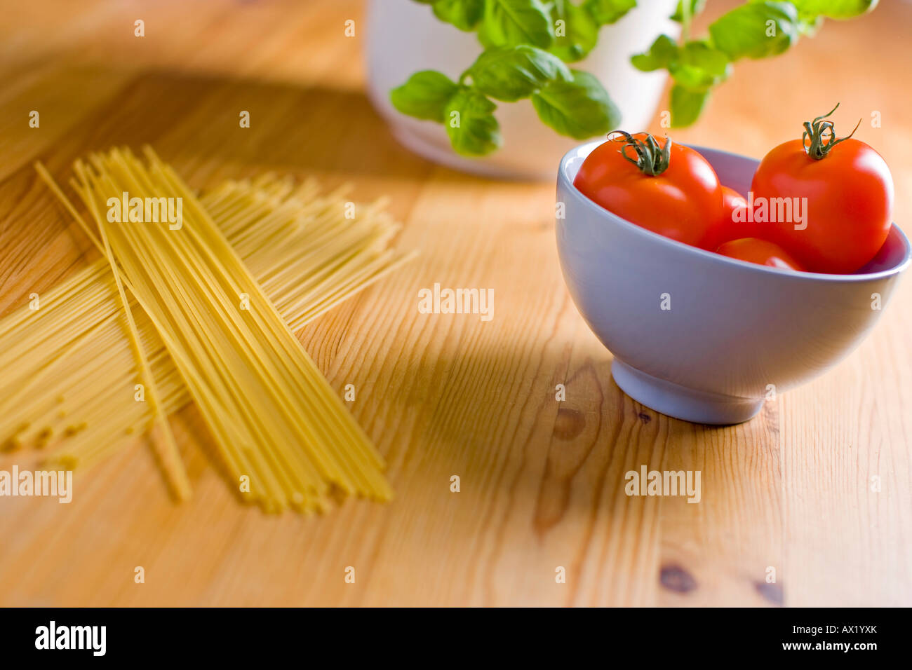 Spaghetti laying beside tomatoes in a bowl with basil Stock Photo