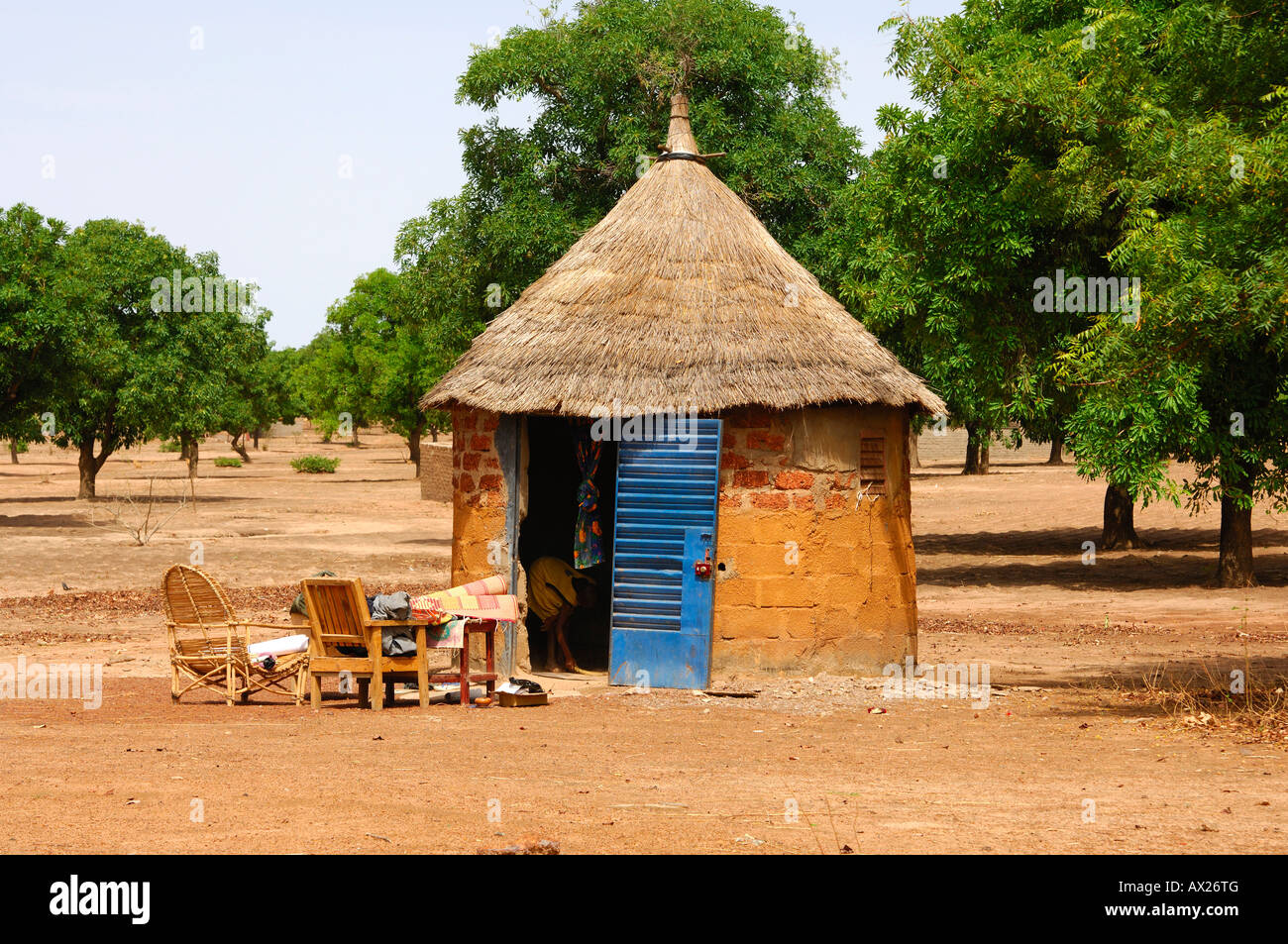 African round hut with thatched roof and interior furniture placed outside during household clean-up, Burkina Faso Stock Photo