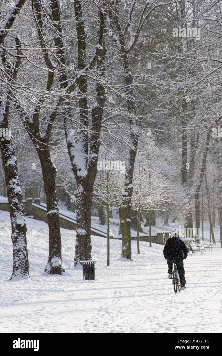 One person riding a bike along a snow covered pathway in winter, in the Arboretum in Lincoln, Lincolnshire Stock Photo
