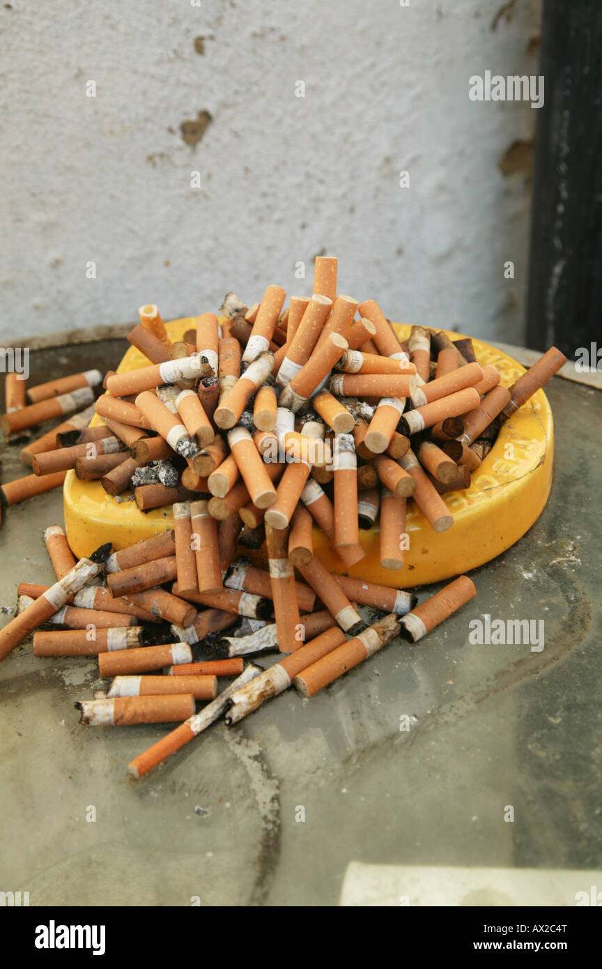 An overflowing yellow ashtray on a table Stock Photo