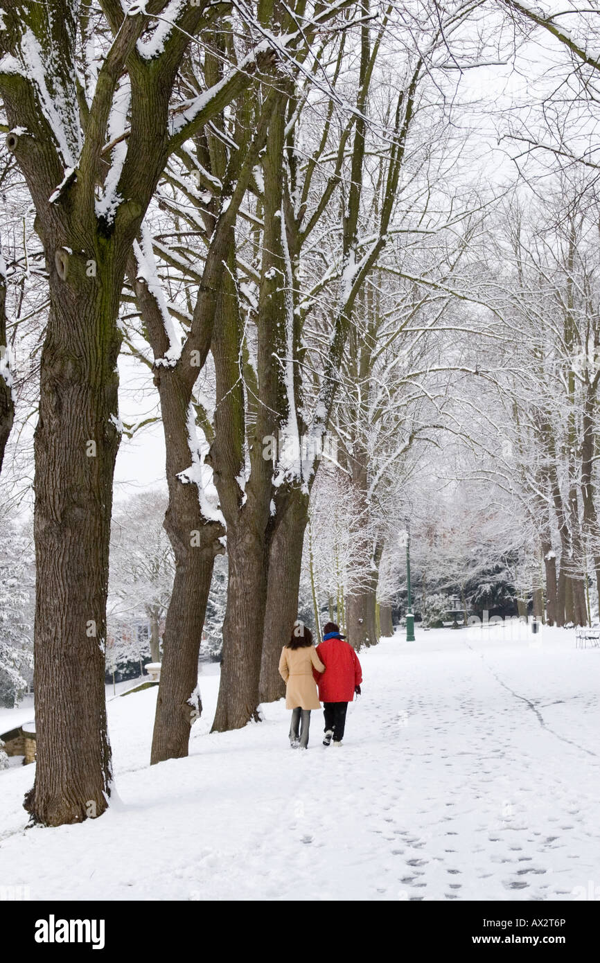 Two people walking  down a snowy path in winter, with trees on either side Stock Photo