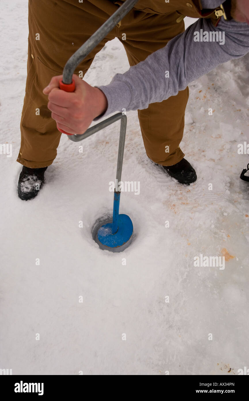 A MAN DRILLS A HOLE THROUGH THICK ICE WITH MANUAL ICE AUGER Stock Photo
