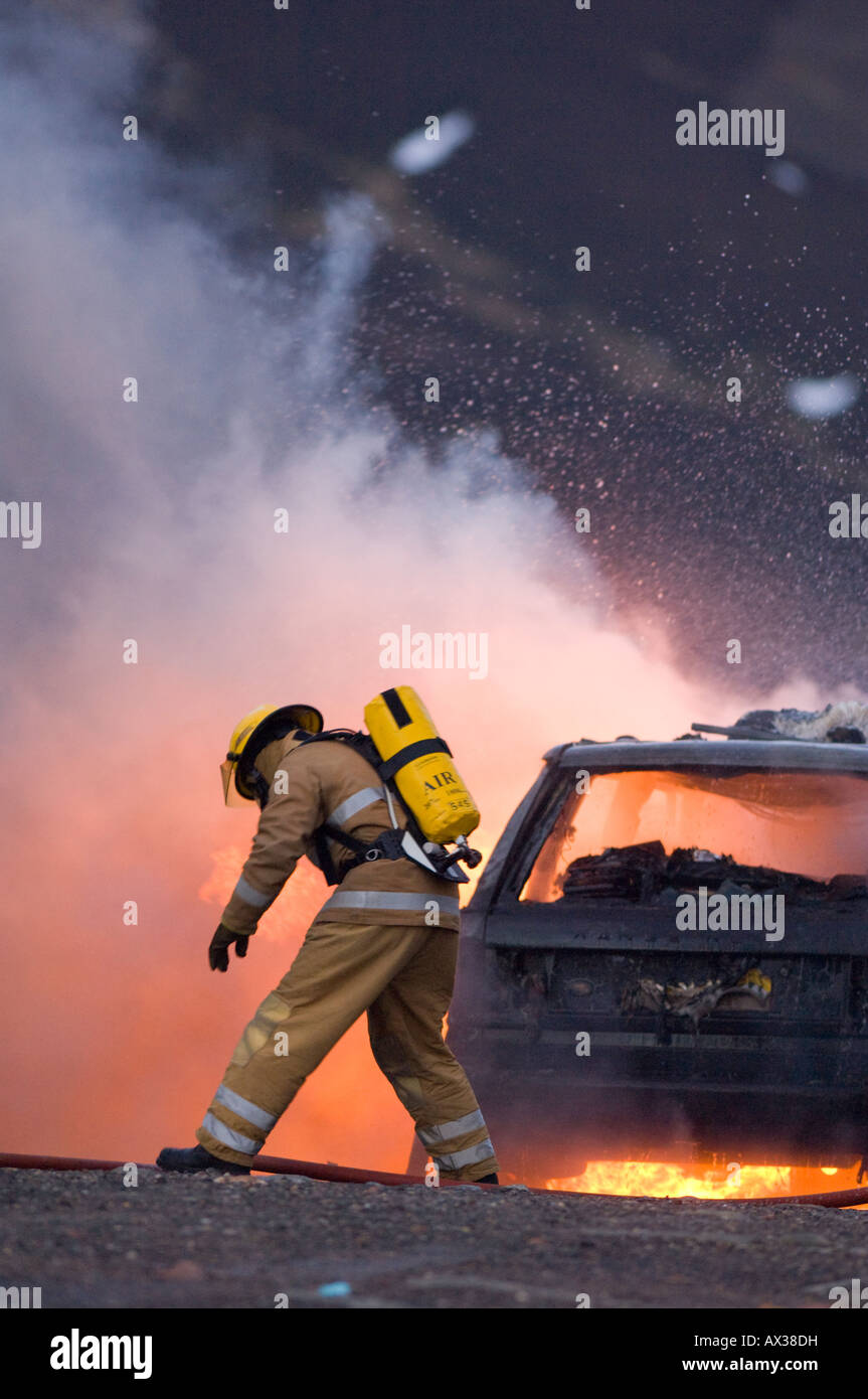A firefighter wearing breathing apparatus tackling a burning car Stock Photo