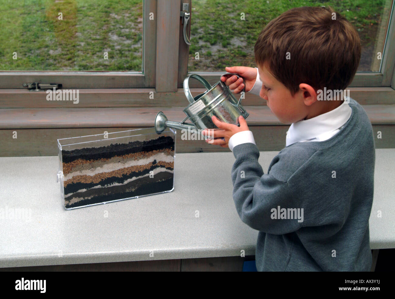 A primary school pupil  adding water to a wormery using a watering can Stock Photo