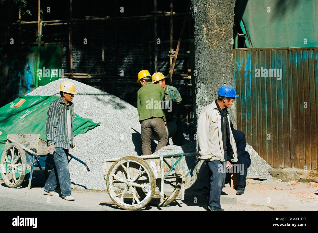 China, Beijing. Construction workers carrying wheel barrows. Stock Photo