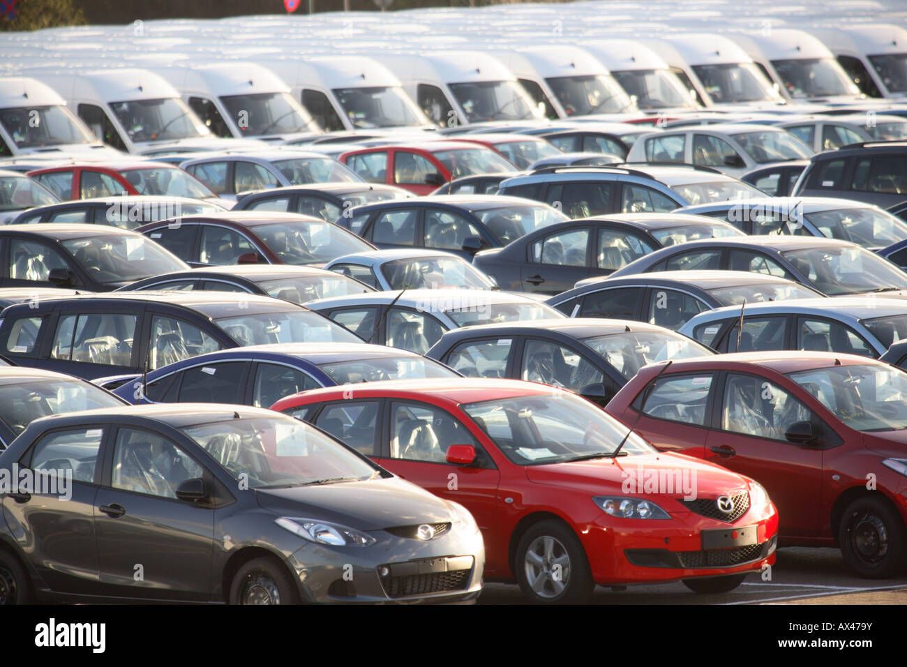 Rows of brand new cars and vans in a car lot awaiting distribution Stock Photo