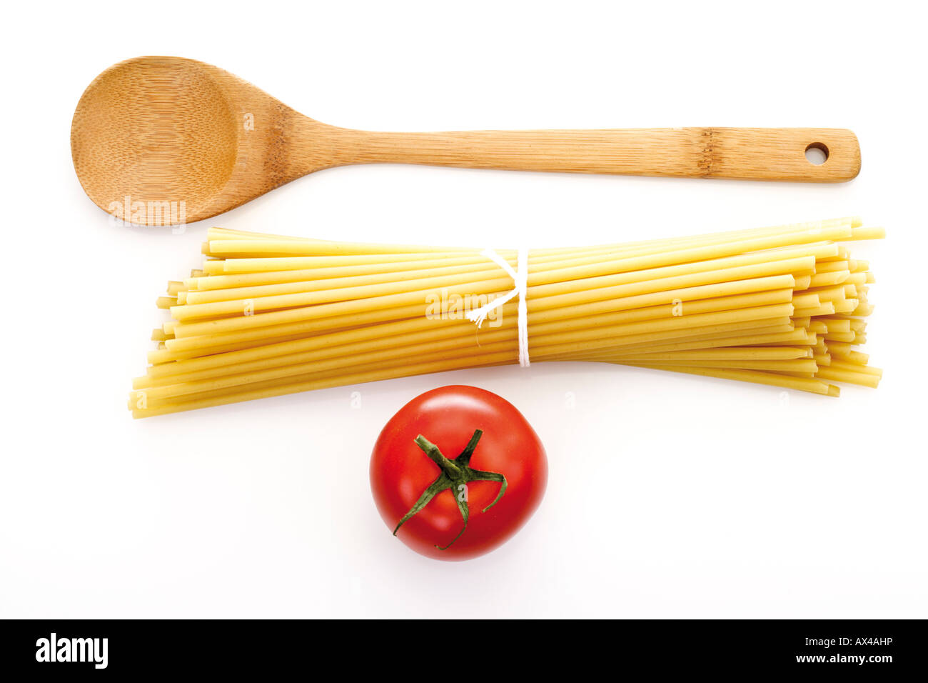 Bundle of spaghetti, wooden spoon and tomato, elevated view Stock Photo