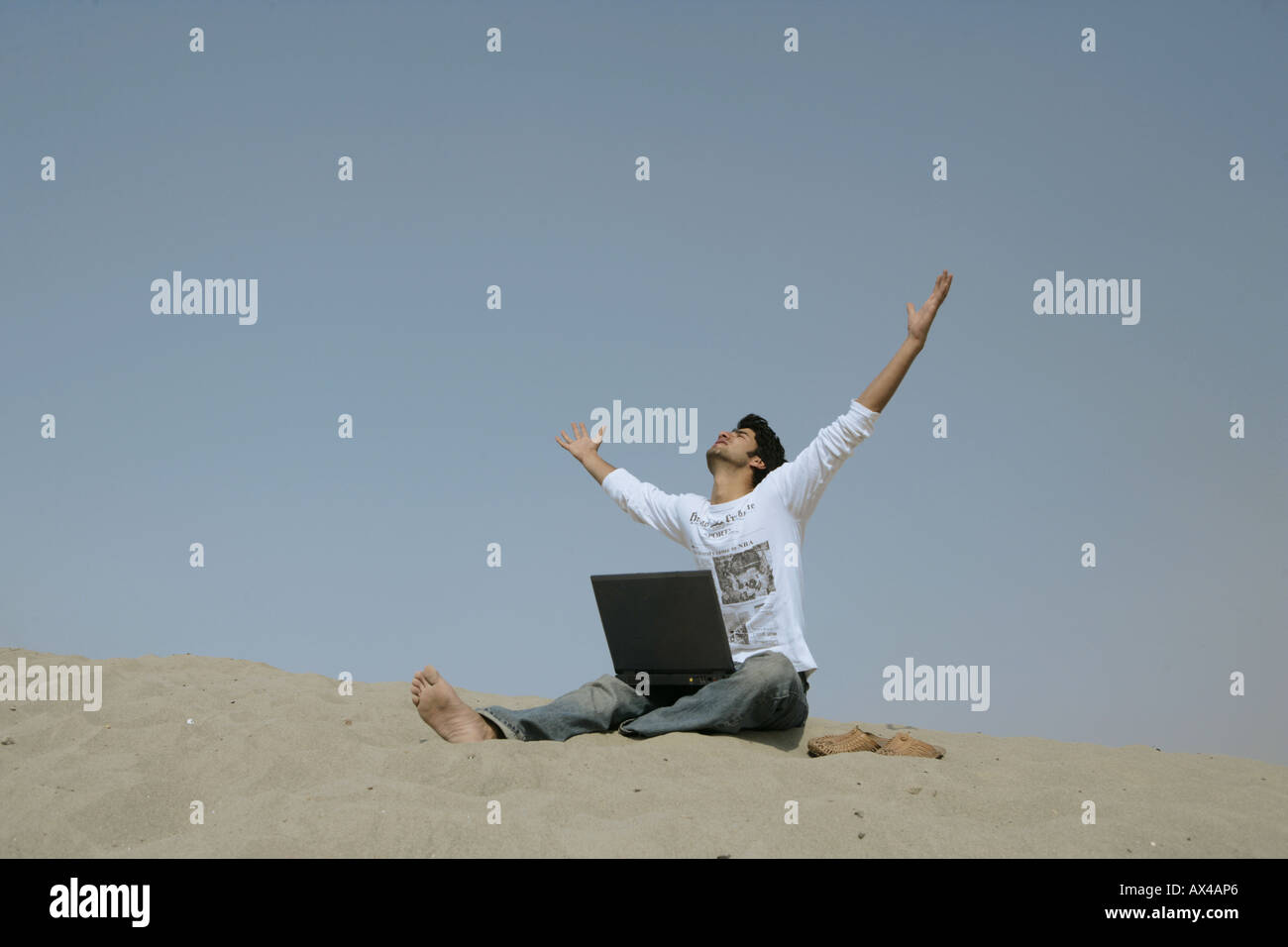 Low angle view of a man sitting on sand in a desert with his arms outstretched Stock Photo
