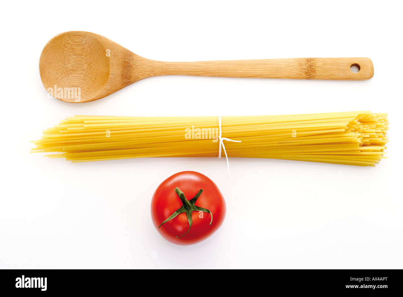 Bundle of spaghetti, wooden spoon and tomato, elevated view Stock Photo