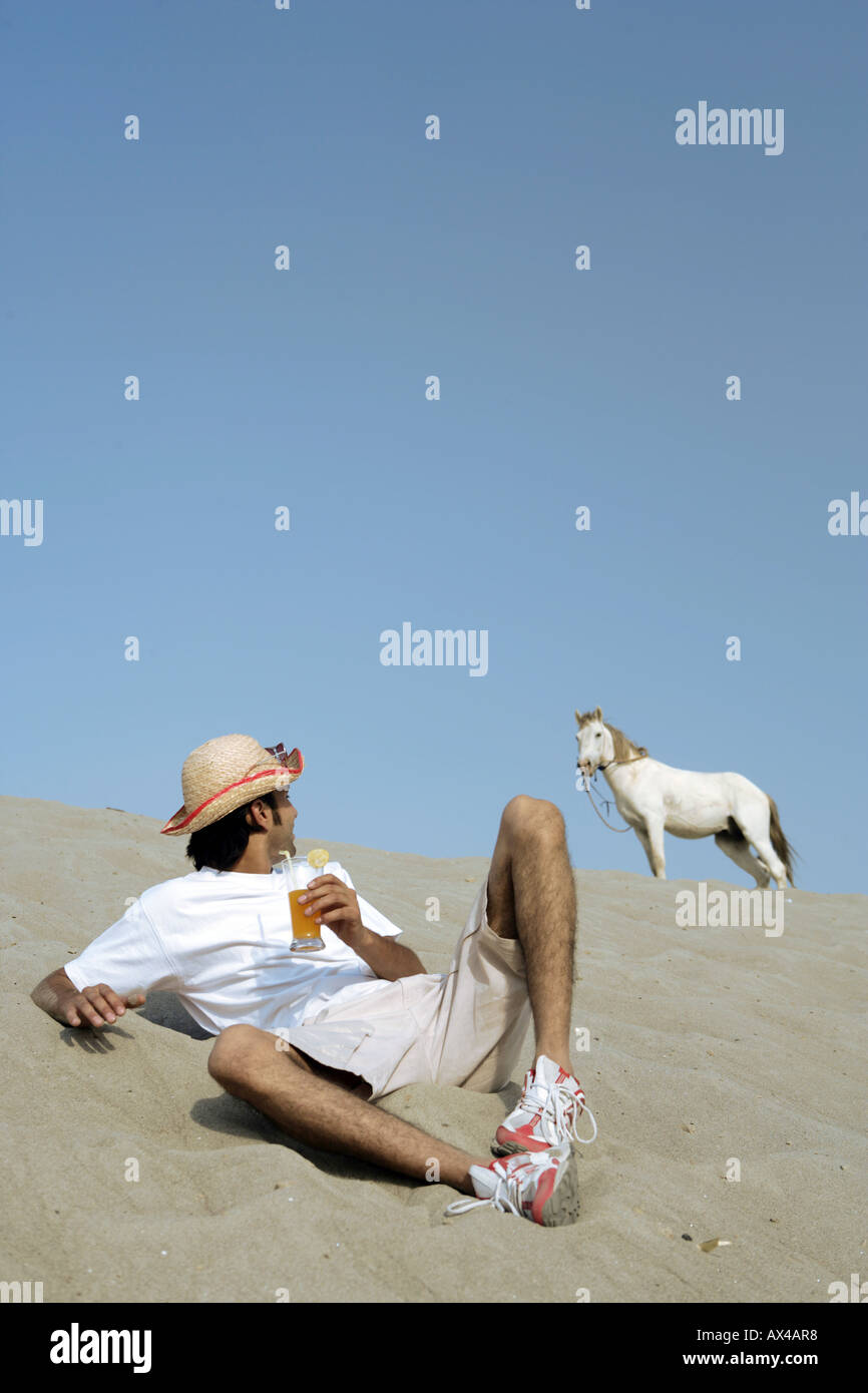 Man sitting on sand in a desert and watching his horse Stock Photo