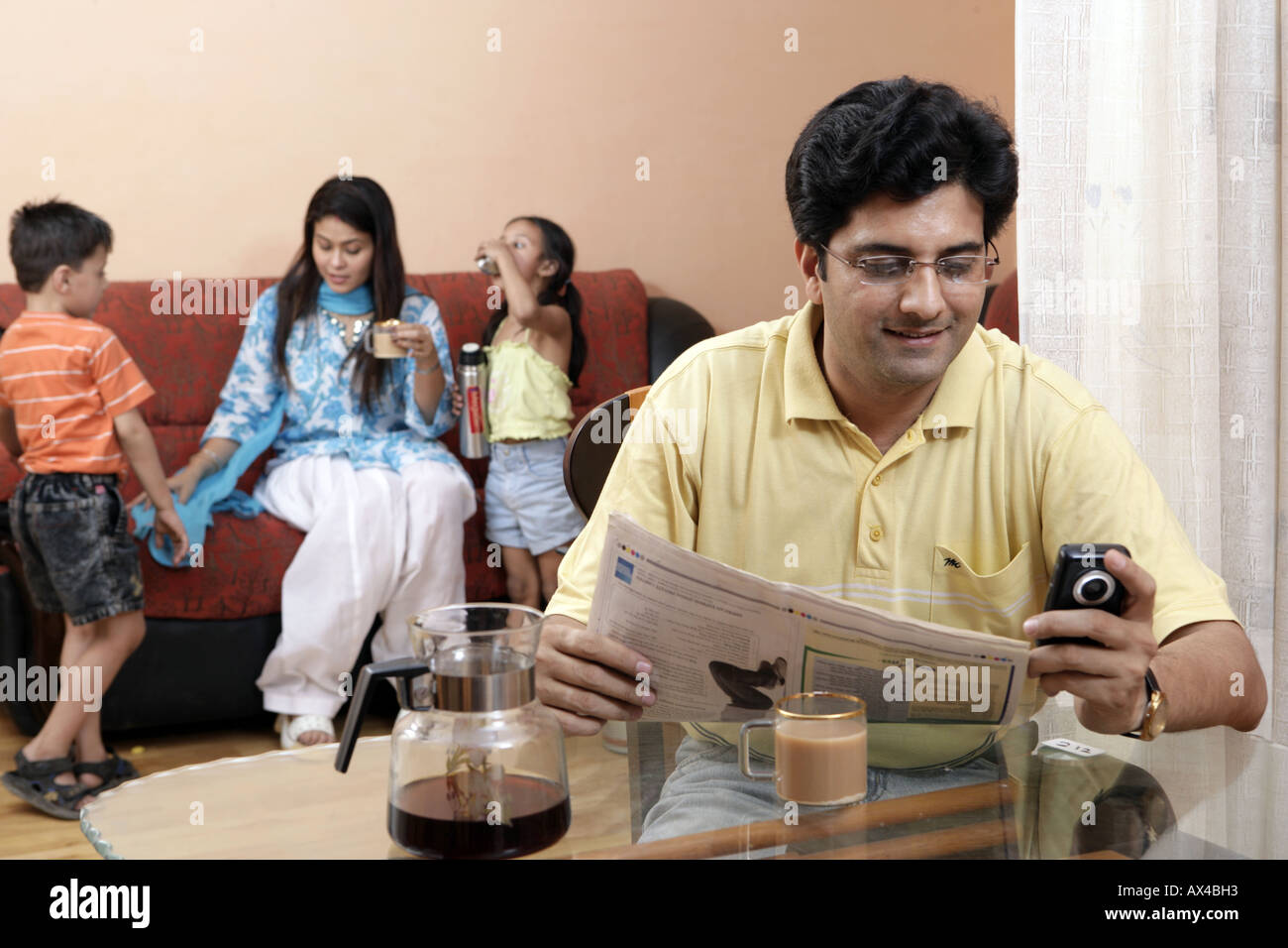 Adult man reading newspaper at dining table with his family sitting in the background Stock Photo