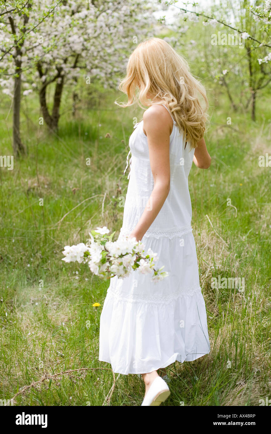 Blonde Woman Dressed In White Walking On The Park With Flowers In Her 