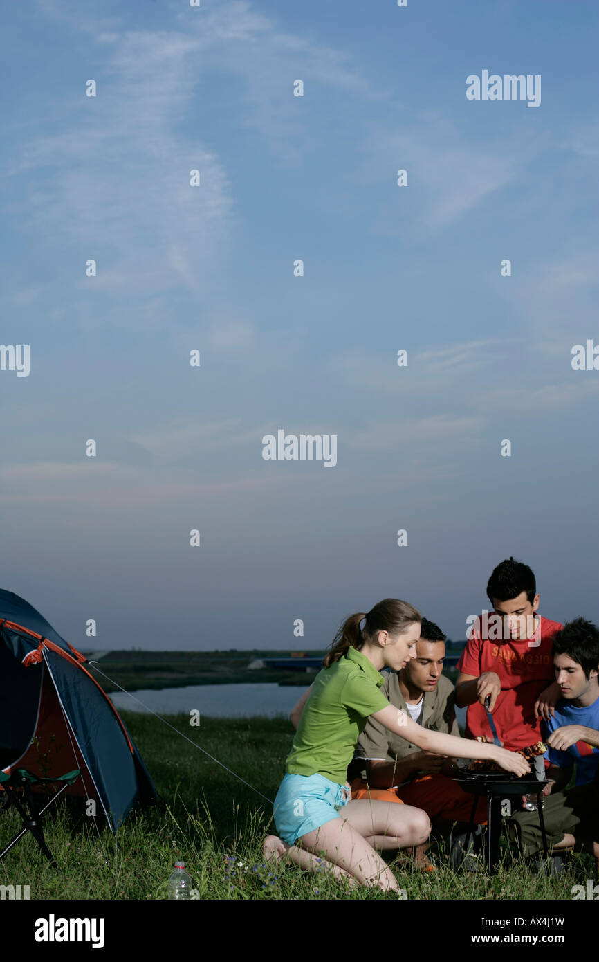 Four young people grilling close to a tent Stock Photo