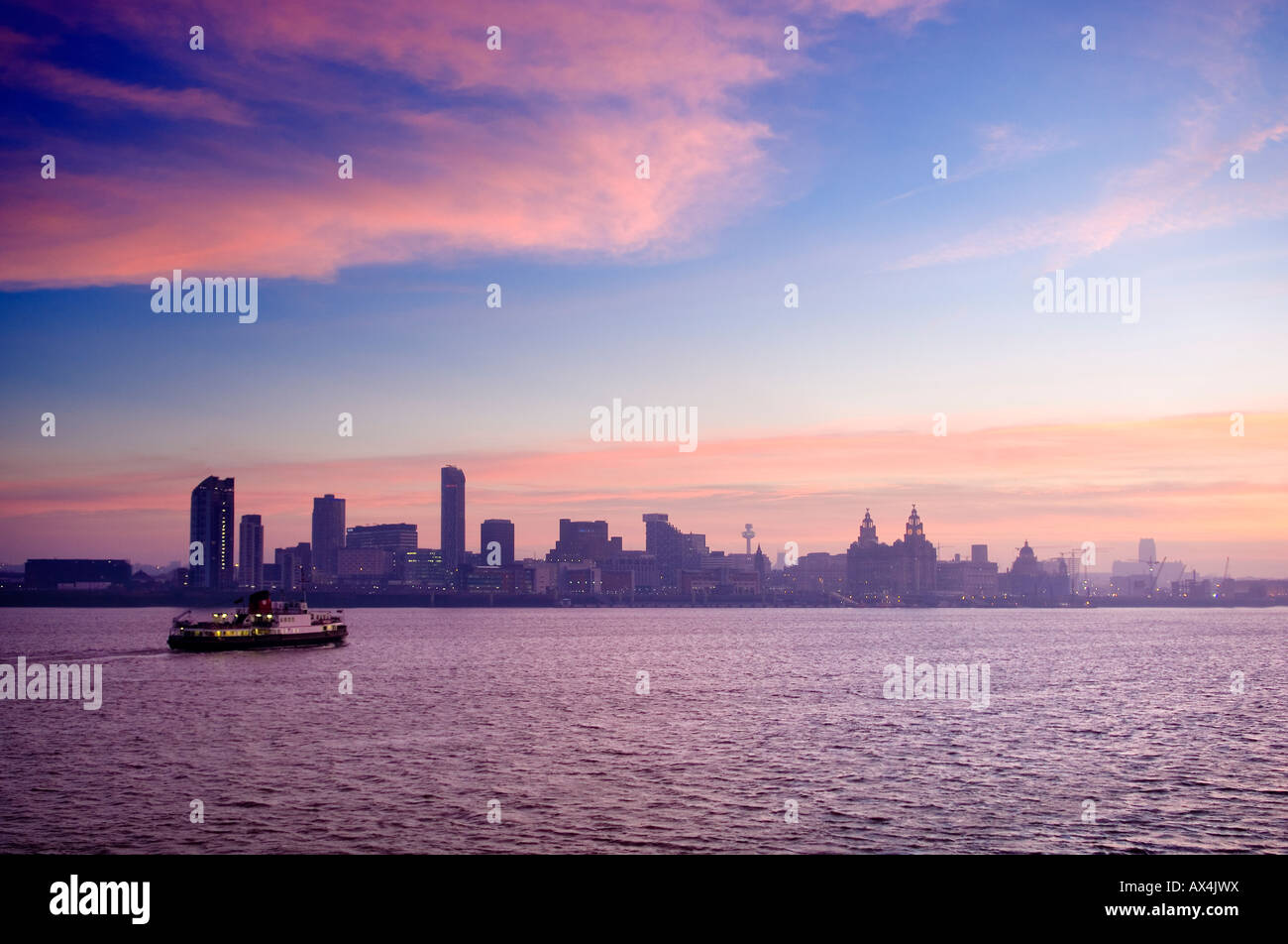 On an early misty morning the Liverpool ferry makes its first trip across the River Mersey. The waterfront skyline visible. Stock Photo