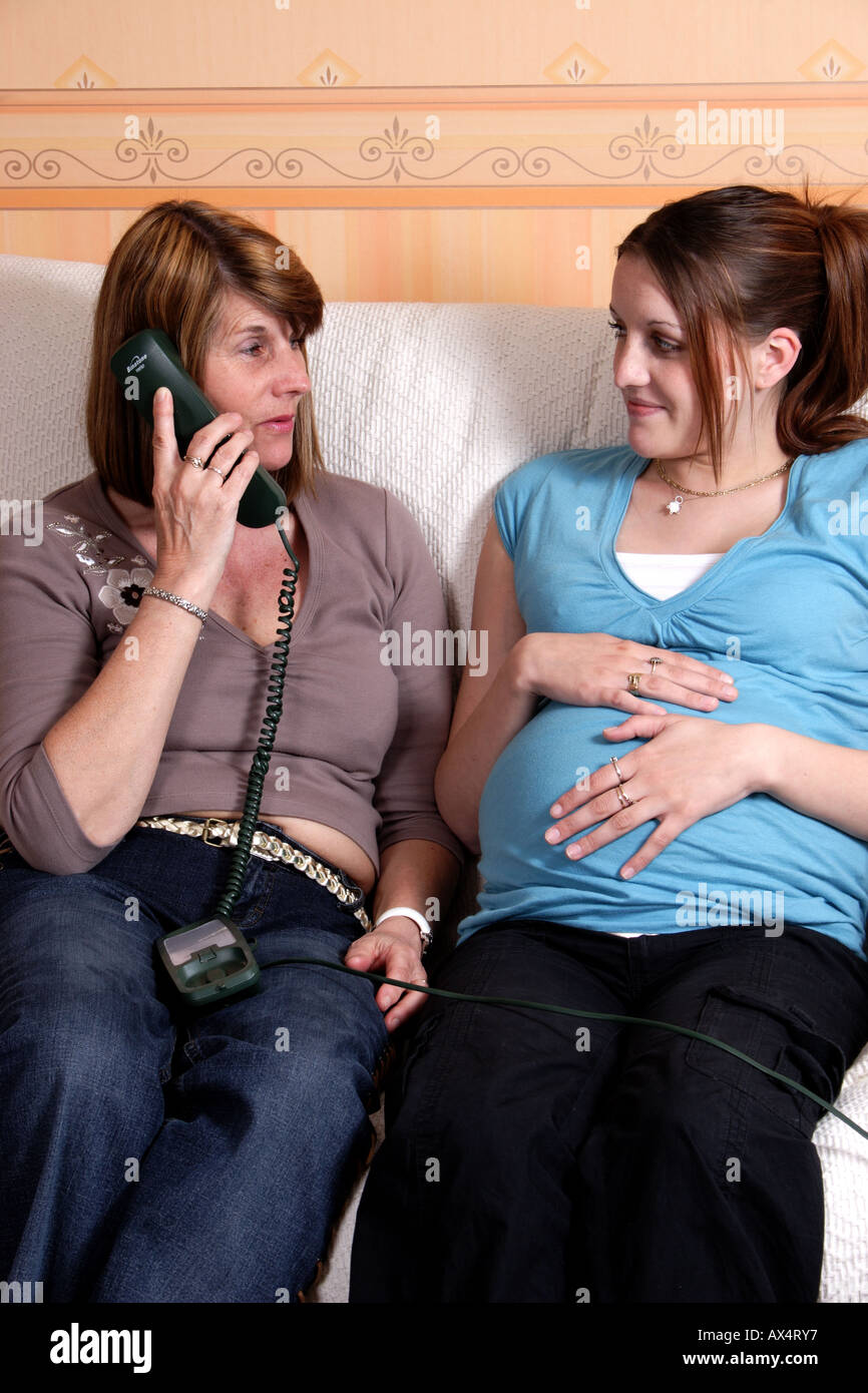 Young heavily pregnant woman with older woman/relative/midwife speaking on telephone Stock Photo