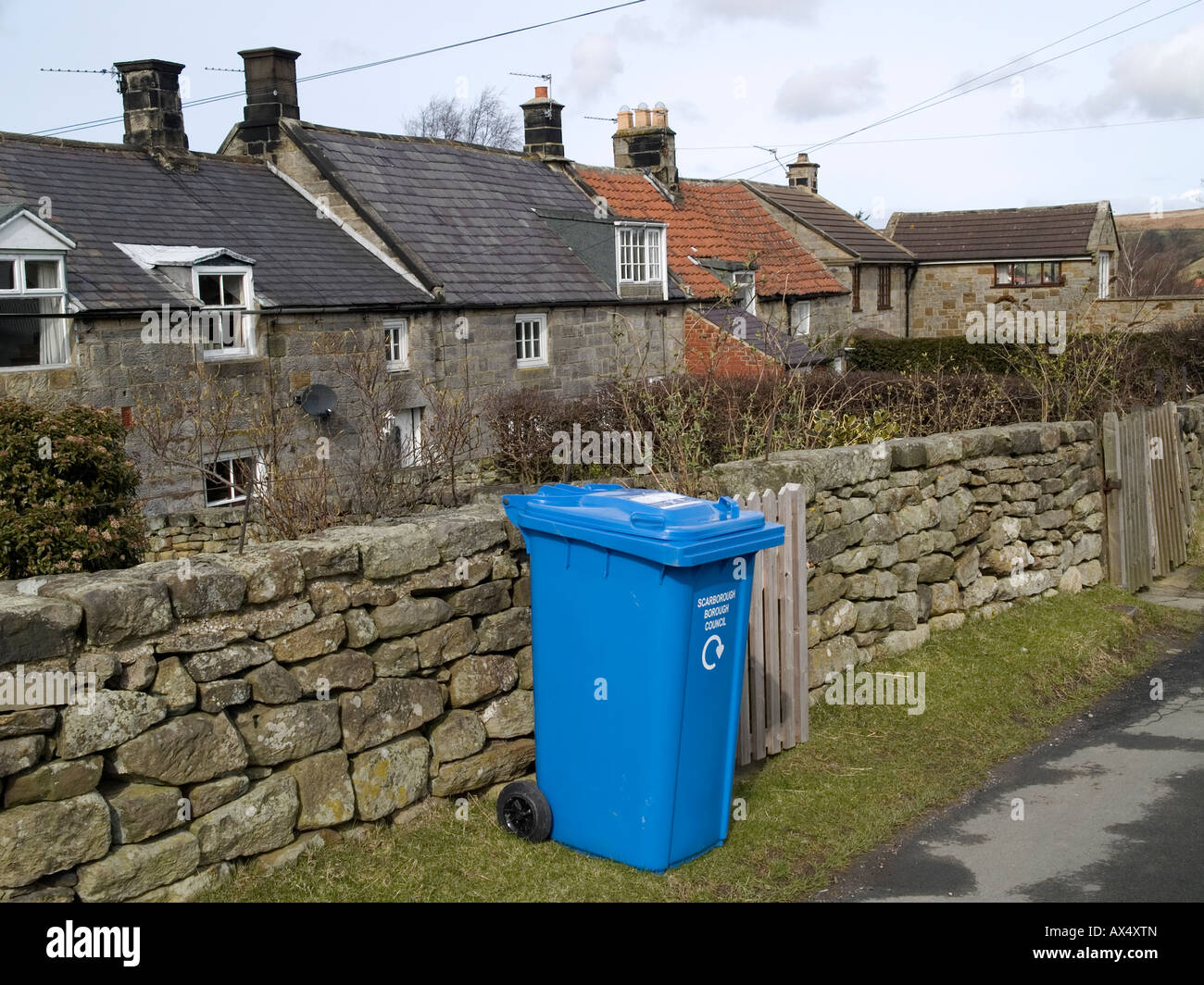 A bright blue wheelie bin for waste disposal outside a row of stone