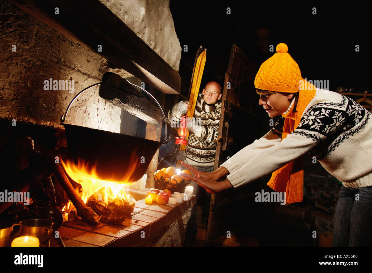 Mid adult couple in alpine hut, woman warming hands at fireplace Stock Photo