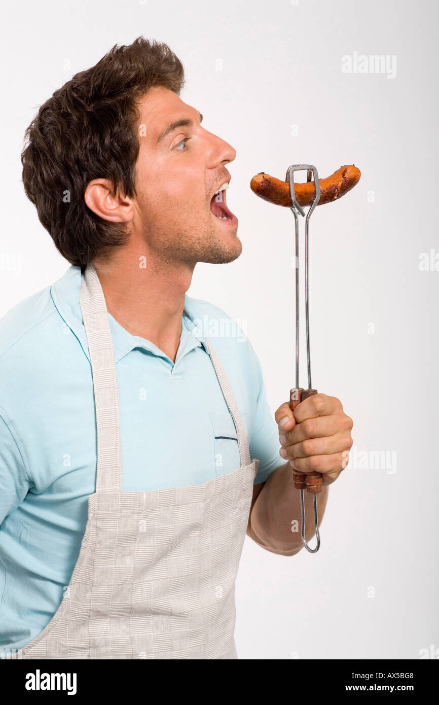 Young man holding grilled sausage, close up Stock Photo