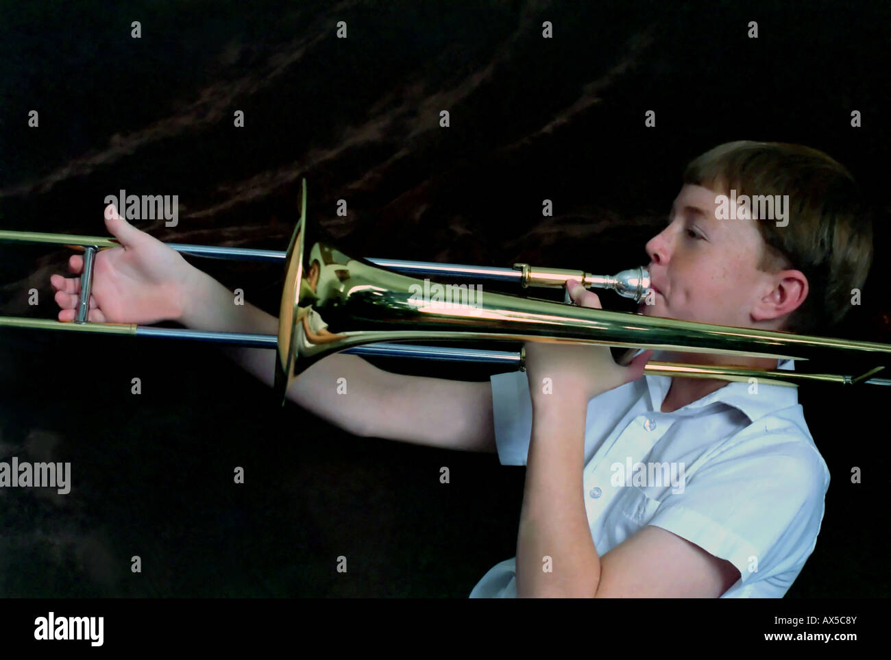 An 11 year old boy playing, or trying to play, the trombone. The musical instrument is almost bigger than he is. Stock Photo