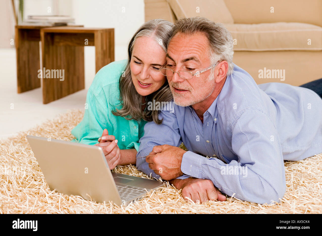 Mature couple in living room, lying on floor with laptop Stock Photo