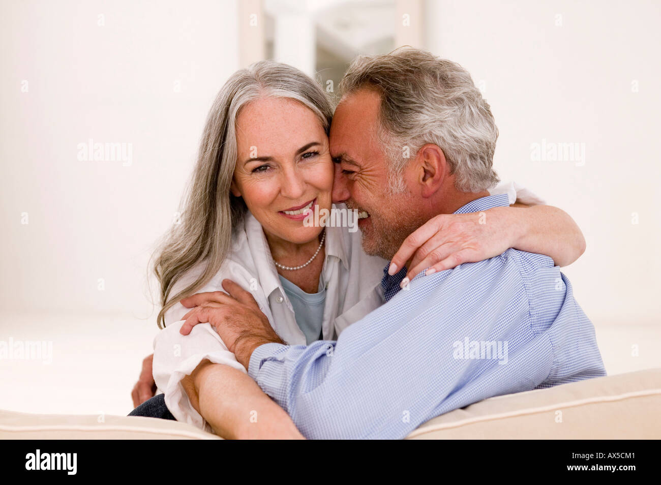 Mature couple embracing on sofa, smiling Stock Photo
