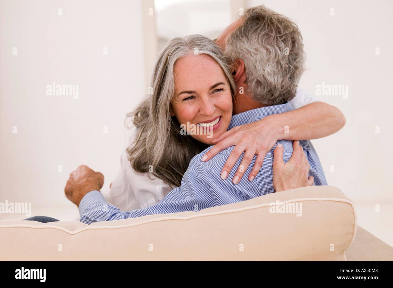 Mature couple embracing on sofa, smiling Stock Photo