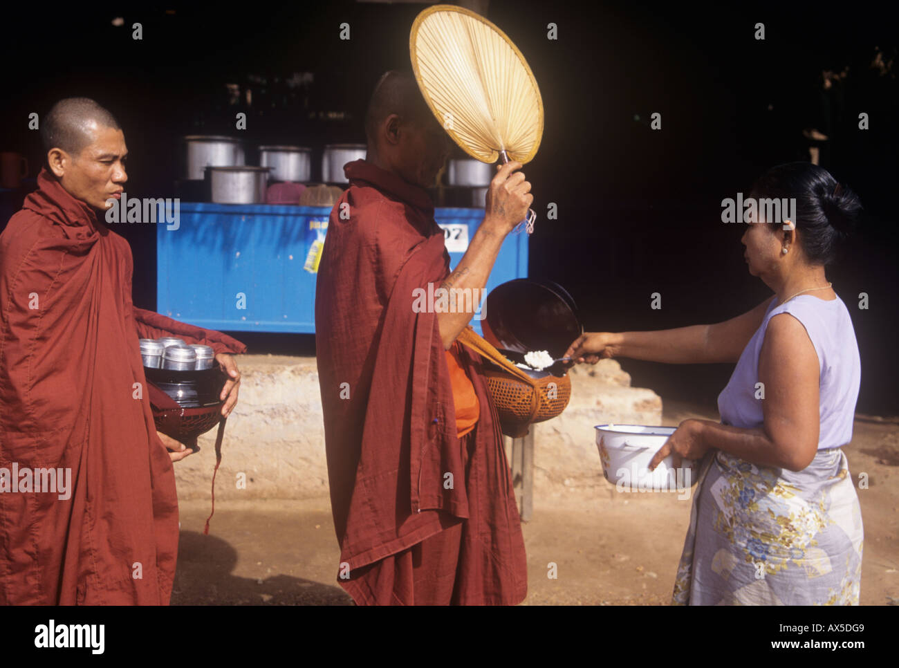 A Burmese village woman giving rice to monks making an alms round in ...