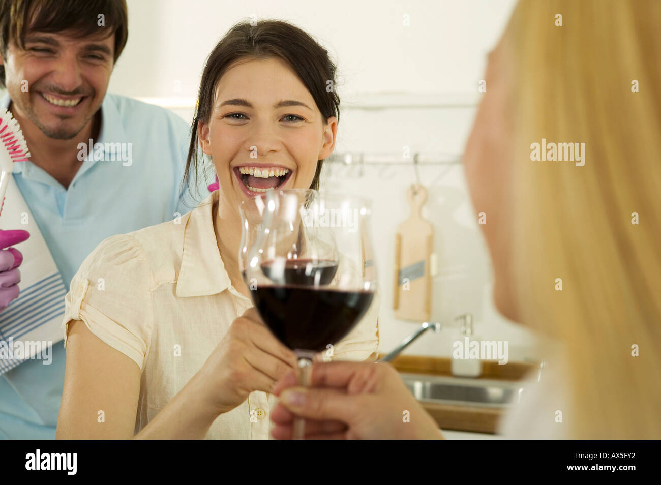 Three young people drinking wine in kitchen, smiling, closeup Stock
