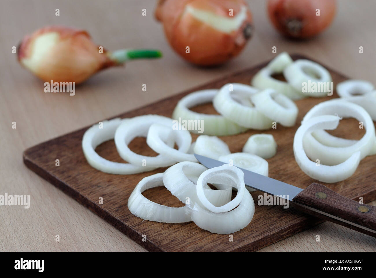 Sliced onions on a wooden cutting board, whole onions in the background Stock Photo