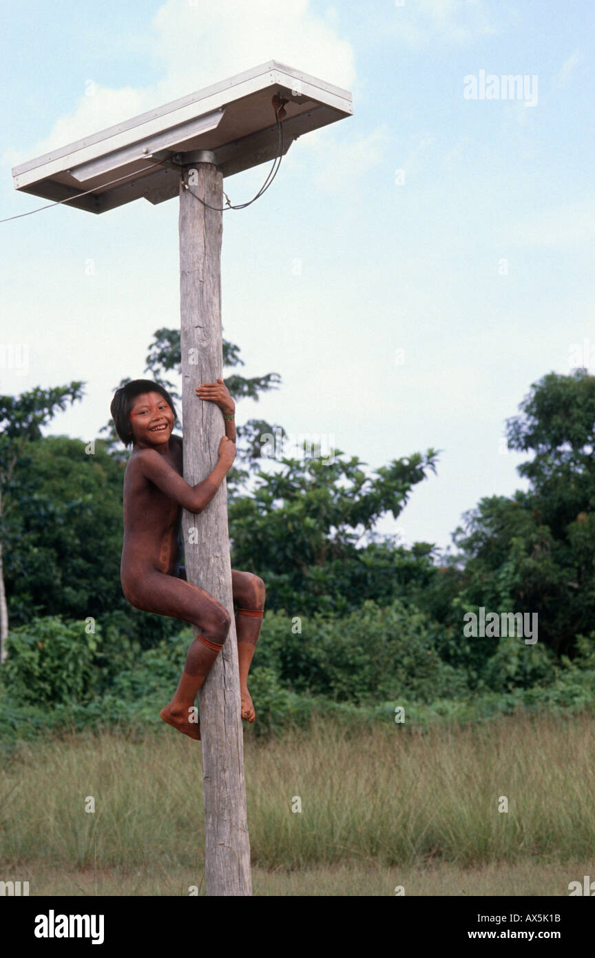A-Ukre Village, Xingu, Brazil. Kayapo girl climbing pole which supports a solar panel power for medical post fridge. Stock Photo