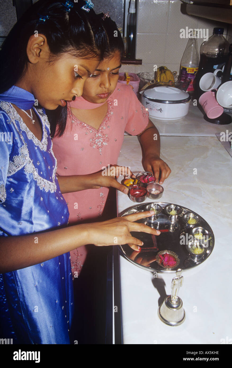 Two Hindu sisters prepare a puja tray to offer at their small family shrine in London Stock Photo