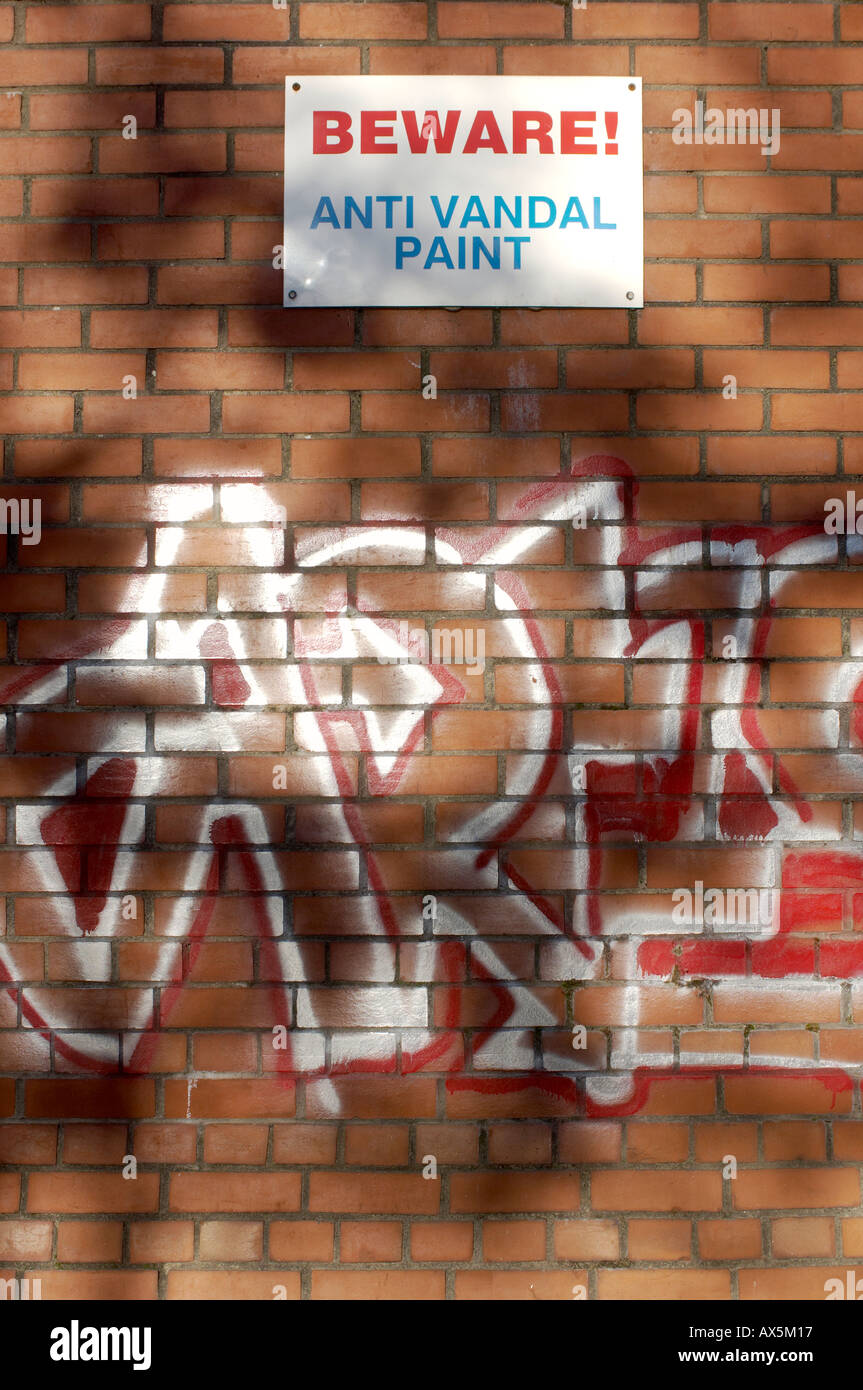 Beware Anti Vandal Paint sign on a graffitied brick wall Stock Photo