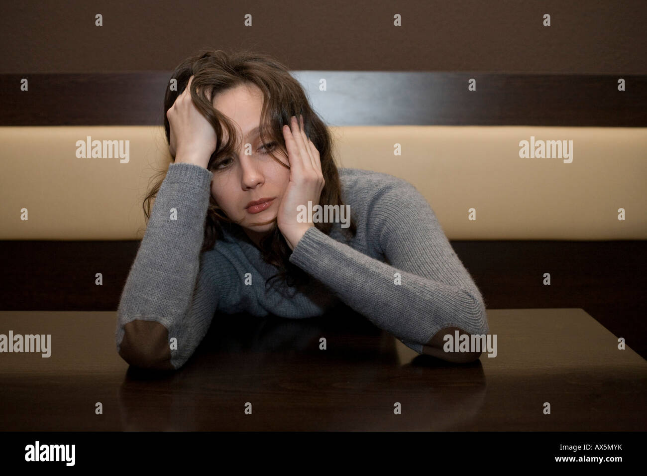Young woman sitting at a table at a bar, looking depressed Stock Photo