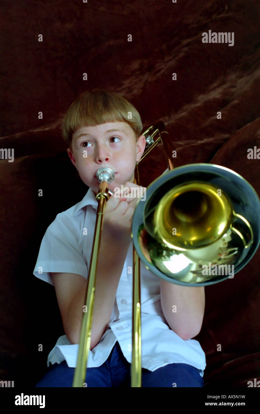 An 11 year old boy playing, or trying to play, the trombone. The musical instrument is almost bigger than he is. Stock Photo