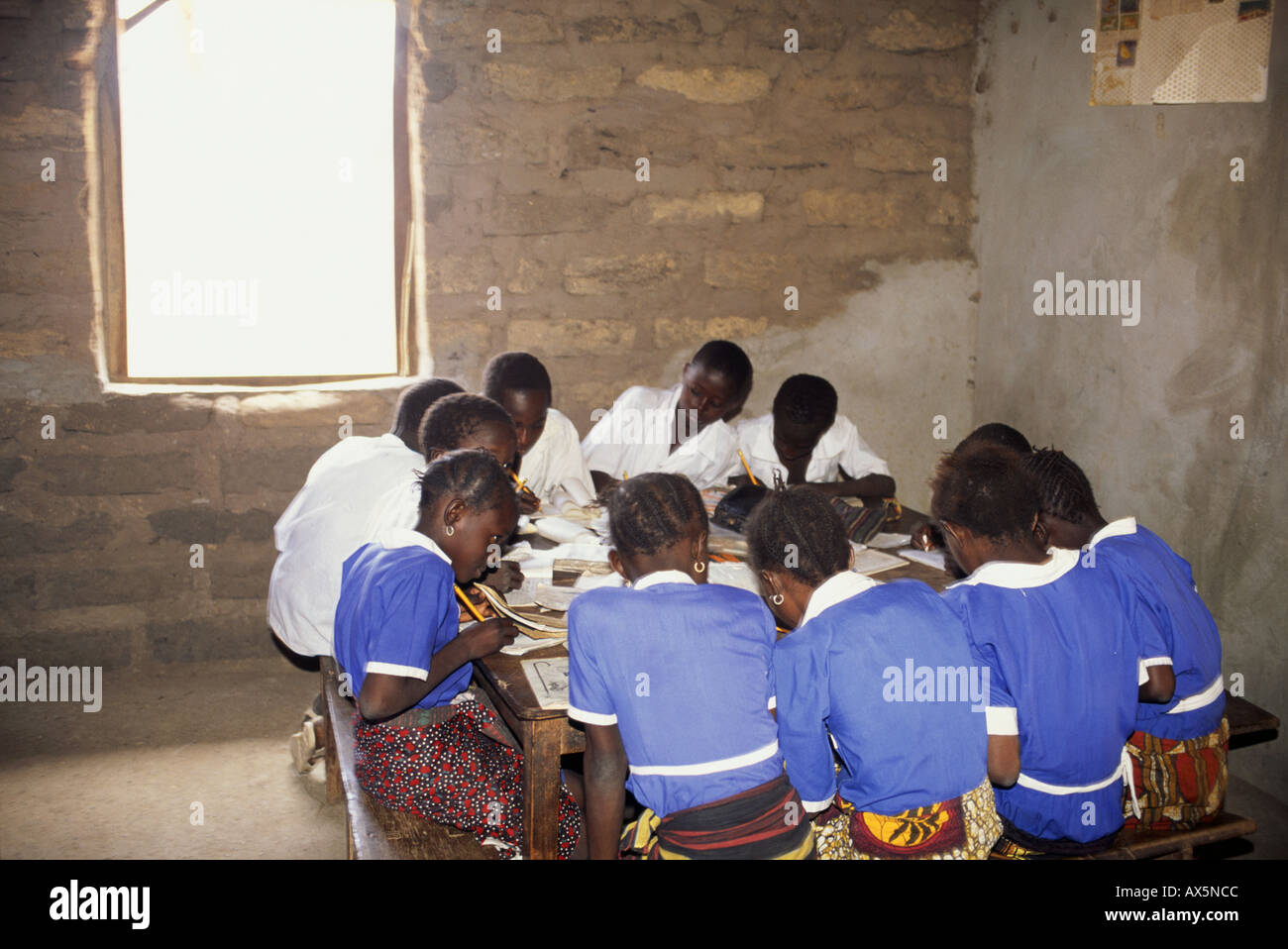 The Gambia. Schoolchildren sitting round a table in a mud brick school room working at their exercise books. Stock Photo