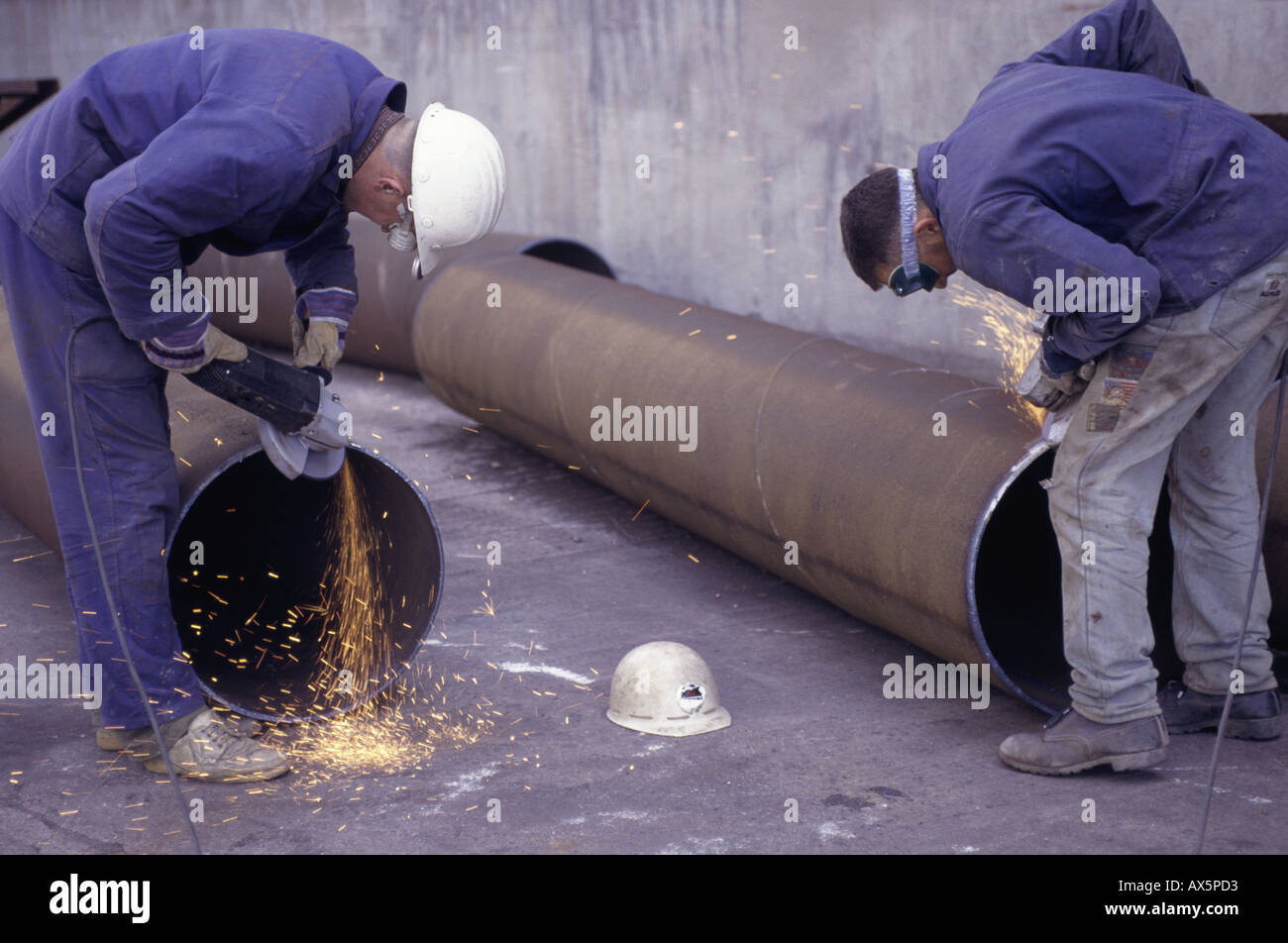Pocerady, Czech Republic. Workers using angle grinders to clean the ends of steel pipes for welding at the power station. Stock Photo