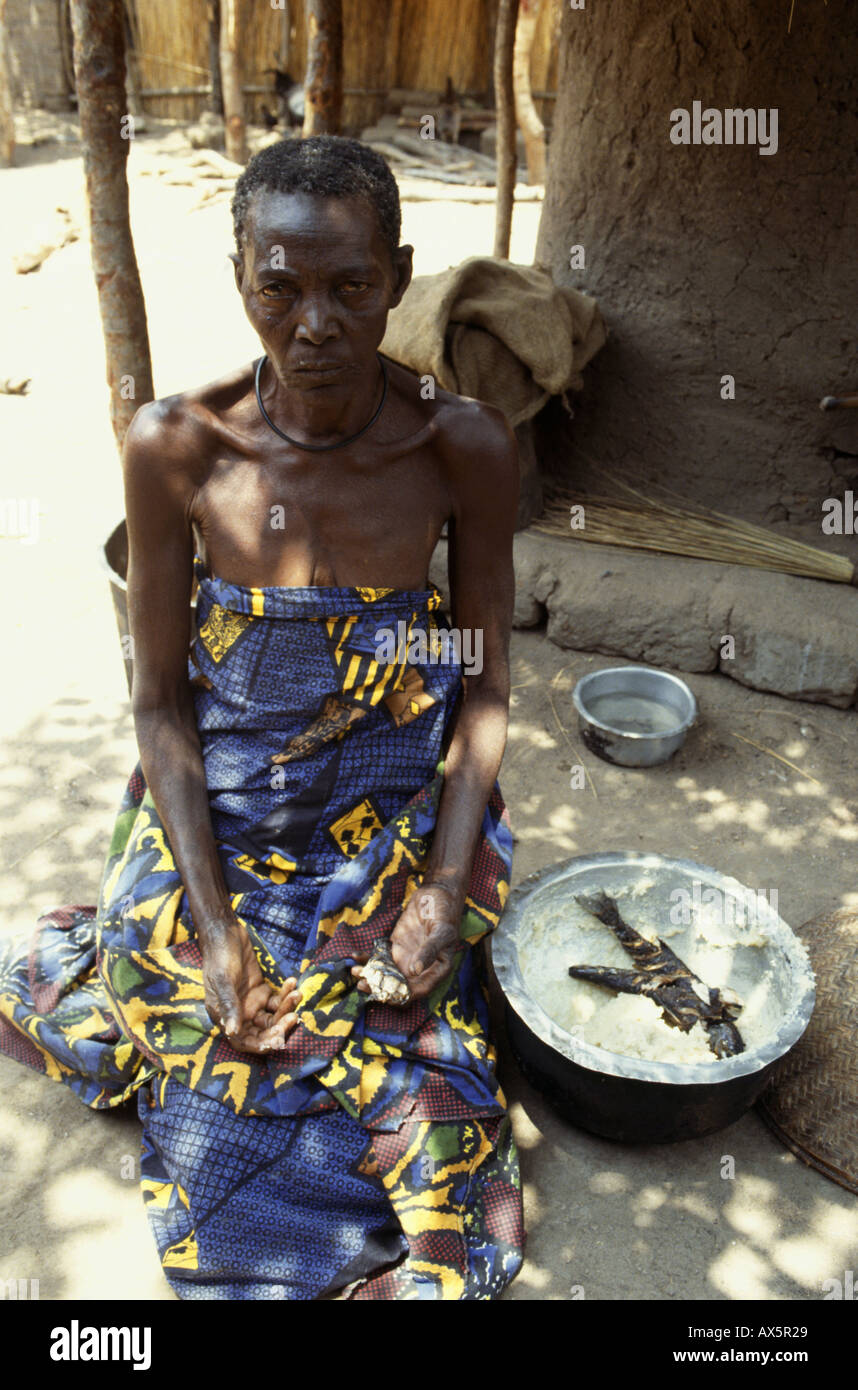 Izinga, Tanzania. Emaciated old woman with bowl of cereal paste with fish outside a mud walled hut. Stock Photo