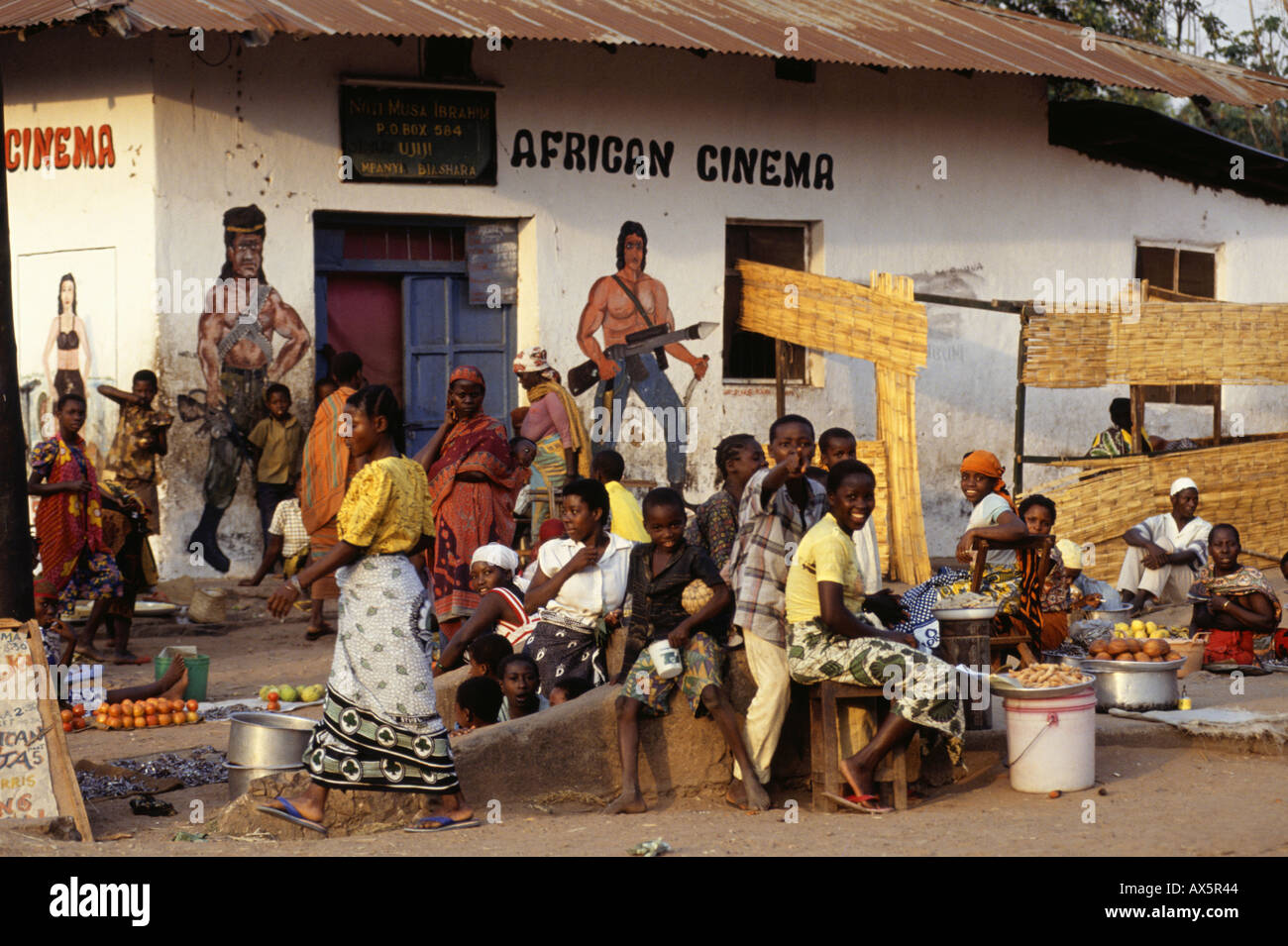 Ujiji, Tanzania. African Cinema with murals of Rambo; food market in front. Stock Photo