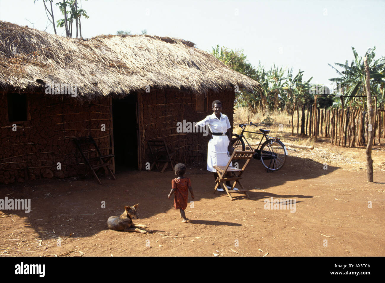 Near Ujiji, Tanzania. District nurse in white uniform with her bicycle outside a mud and thatch hut. Stock Photo