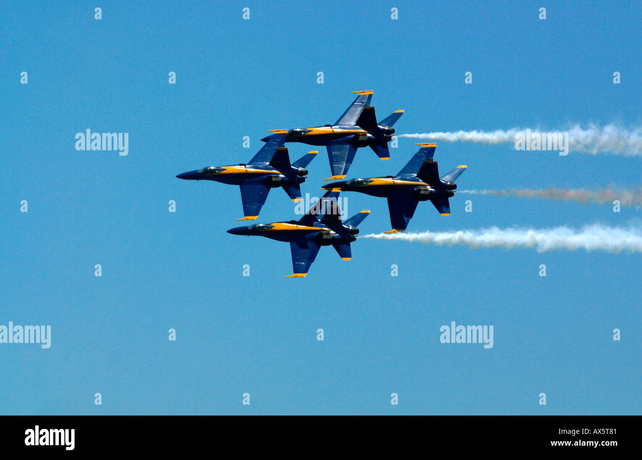 The Blue Angels FA 18s fly in diamond formation with trails of white smoke against a clear blue sky Stock Photo