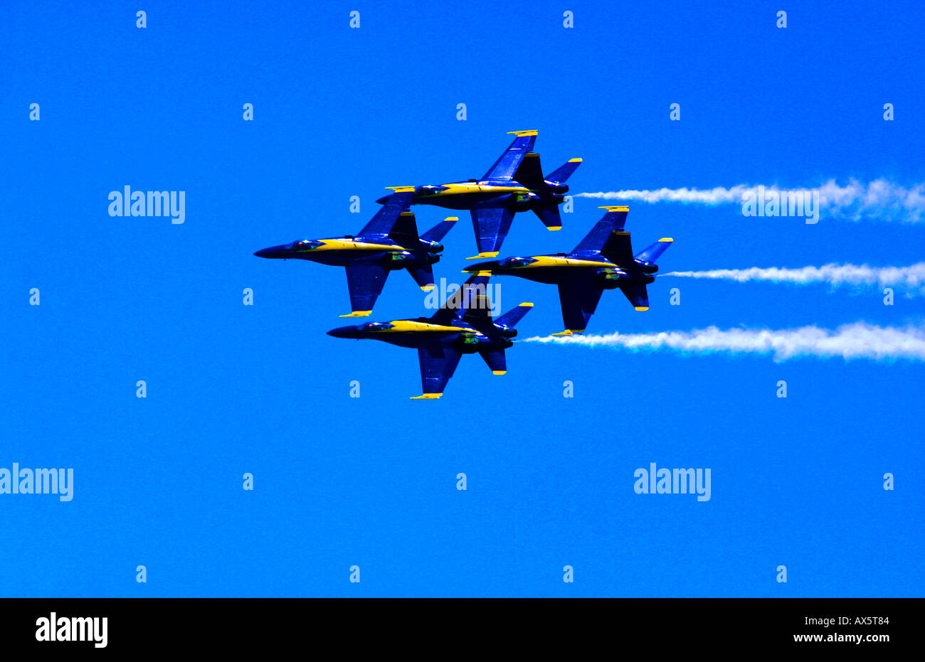 The Blue Angels FA 18s fly in diamond formation with trails of white smoke against a clear blue sky Stock Photo