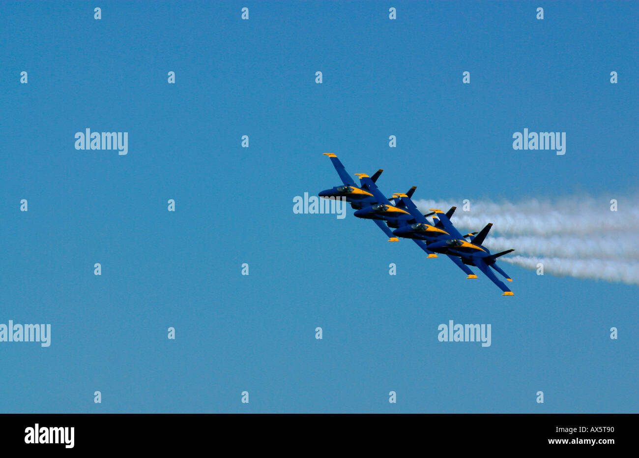 The Blue Angels FA 18s fly in formation with trails of white smoke against a clear blue sky Stock Photo